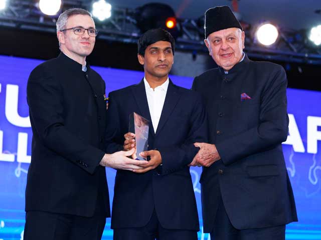 Srikanth Bolla receiving an award on stage, flanked by two dignitaries in suits.