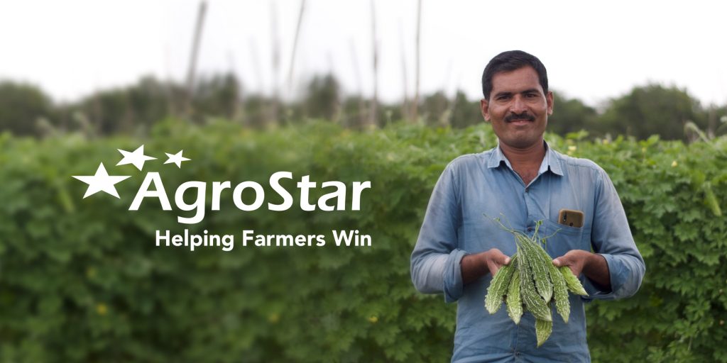 A man standing in a green field holding fresh produce with an AgroStar banner in the background.