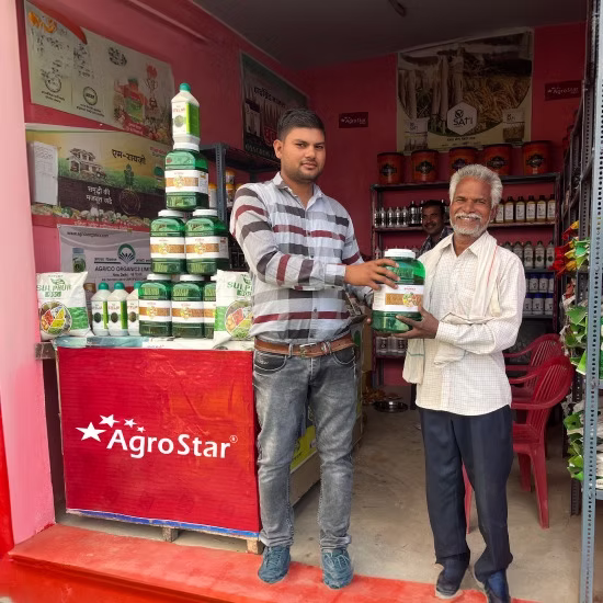 Two men standing inside a shop, holding an agricultural product container in front of a counter with AgroStar branding.