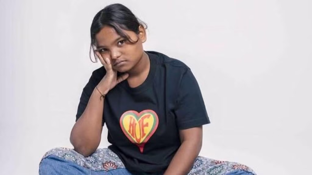 Paramjeet Kaur, 19-year-old Punjabi singer of That Girl, sitting casually in jeans and a black T-shirt with a heart logo, resting her face on her hand against a plain white backdrop.