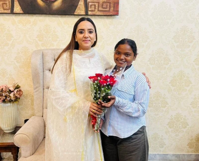 AAP MLA Amandeep Kaur Arora stands beside singer Paramjeet Kaur, holding a bouquet of red roses, both smiling during their meeting indoors.